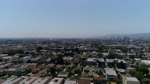 Slow moving drone shot over Los Angeles neighborhood with rooftops, skyline, hills and populated cit