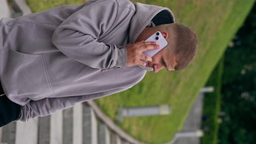 Vidéo verticale Dans le parc Un homme vêtu d'un sweat-shirt gris parle au téléphone après avoir fait du sport