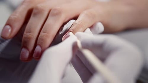 The Manicurist Pushes the Cuticle Away with a Wooden Stick Closeup Cutting Cuticles on Fingers