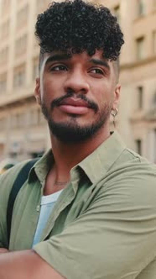 Young happy man stands next to the road, turns his head, crosses his arms and looks at the camera
