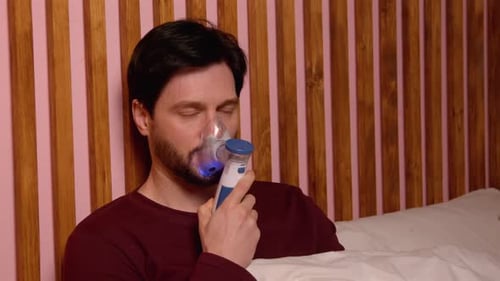 Homme mûr malade traitant des difficultés respiratoires avec un inhalateur pour asthme à l'intérieur