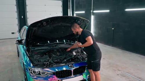 Ein Autoservice-Mitarbeiter schaut auf ein Tablet in seiner Hand, während er neben einem teuren Auto steht
