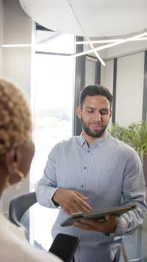 Vertical video: Discussing project details, man holding tablet and talking to colleague in office