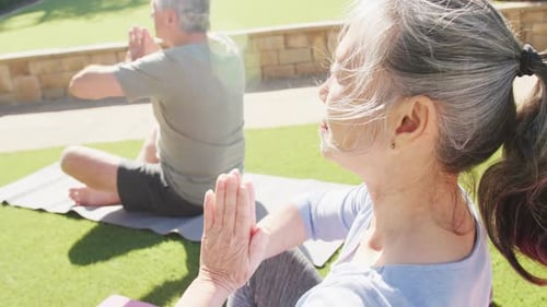 Happy diverse senior couple practicing yoga and meditating on mats in garden