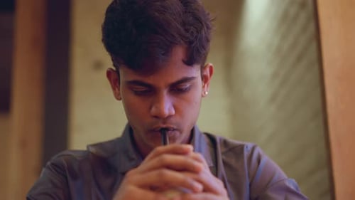Centered Front View of Young Man Drinking Through Black Straw with Eyes Looking Downward