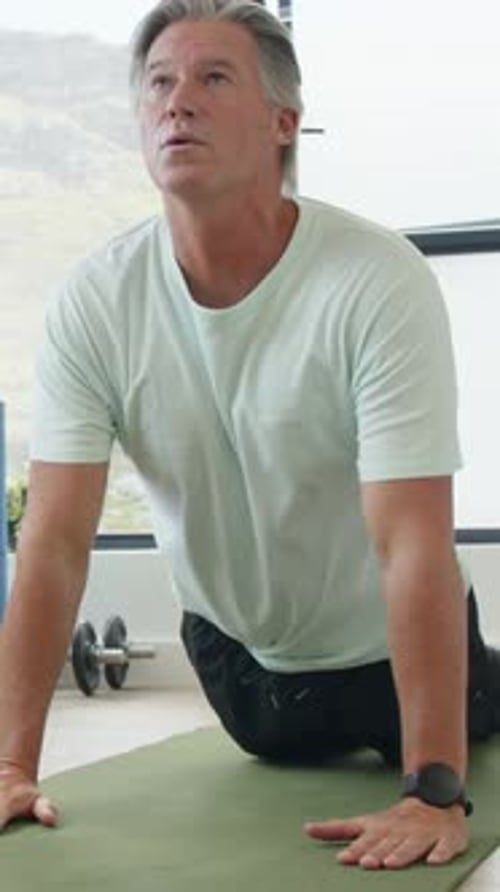 Vídeo vertical: Presionando las palmas de las manos, hombre con camiseta color menta, pantalones cortos arqueando la columna vertebral sobre la colchoneta para abrir el pecho