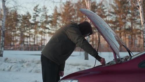 Person Repairs Car Outdoors in Winter