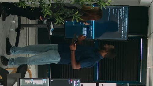 Vídeo vertical: diverso equipo de ingenieros de software analizando el código en un televisor con pantalla de pared