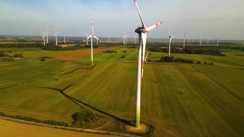 Drone shot of the wind turbines working in a wind farm generating green electric energy on a wide gr