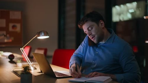 Busy Startuper Talking Cellphone Writing in Notebook at Night Office Closeup