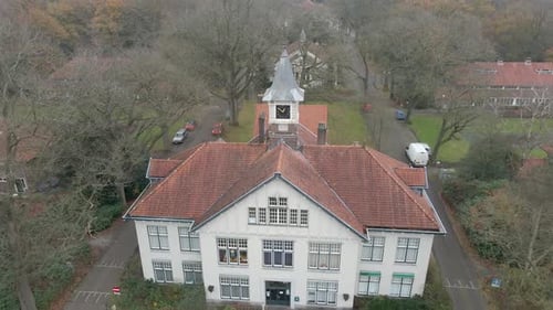 Drone flying away from old mansion with clocktower in autumn