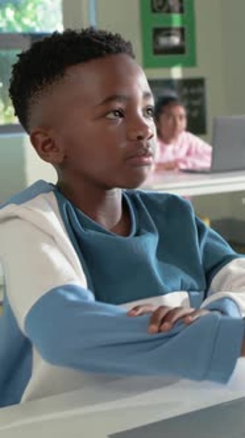 Vertical video: Responding to teacher cue, child in blue tee speaking, turning in class with laptop