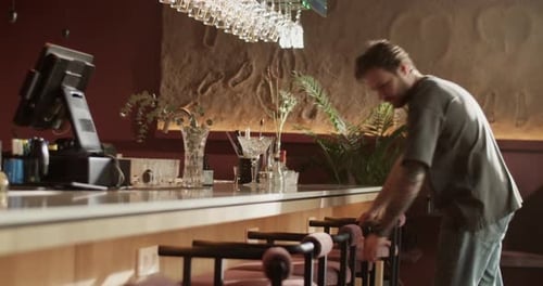 Male Barkeeper Arranging Bar Chairs Before Opening
