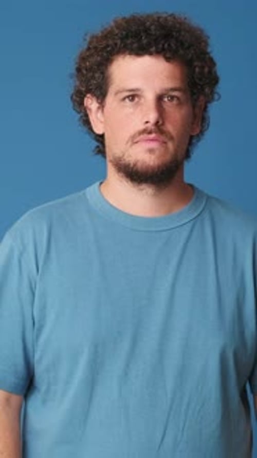 Young man crossing his arms, looking at the camera with smile isolated on blue background studio