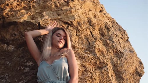 Young Woman in Blue Dress Walking on the Beach with Big Stones and Amazing Sunrise
