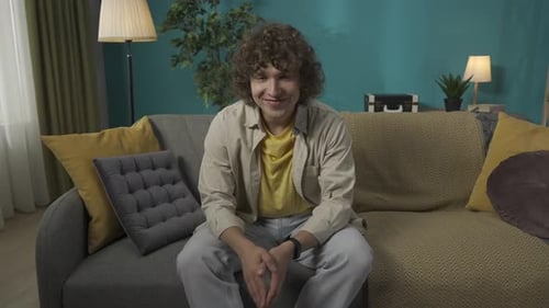 Young Man in Casual Clothing Sitting on the Sofa in the Living Room Looking at the Camera and