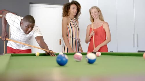 Young African American man plays pool with biracial and Caucasian women
