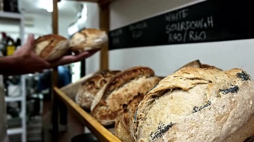 Baker places fresh out the oven sourdough loaves onto a shelf for sale in a bakery