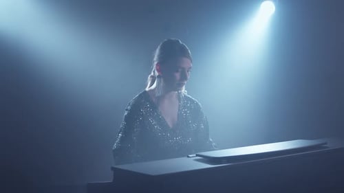 Blonde Woman Plays Piano in Dark Studio