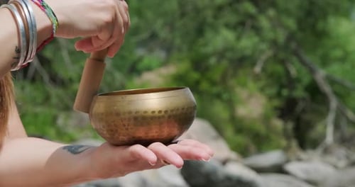 Ringing Tibetan Bell. Female Hand Circling The Rim Of A Bowl With A Baton And Strike. close up