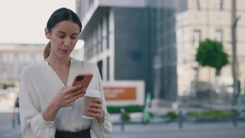 Happy Businesswoman Using Smartphone While Standing Near the Office Building on the Coffee Break
