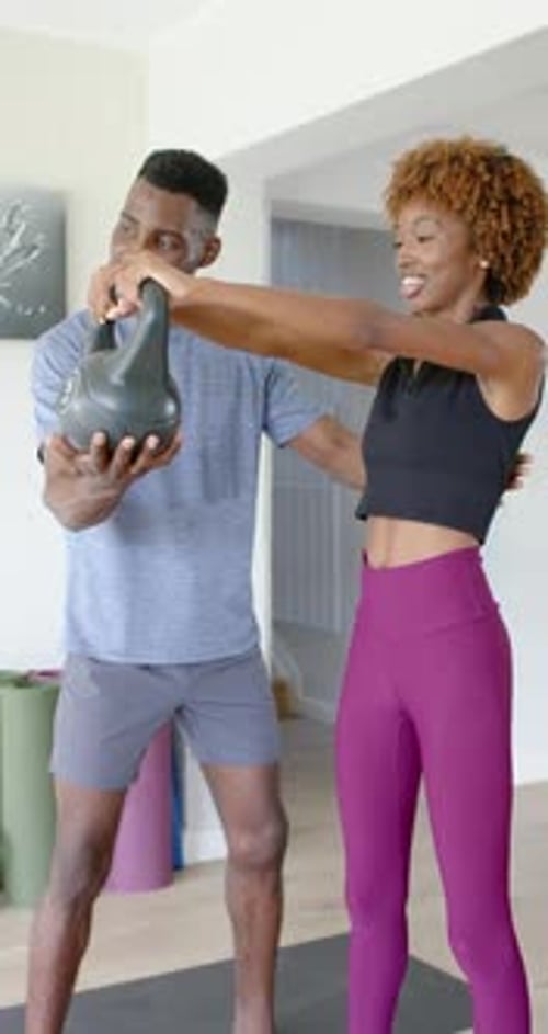 Vídeo vertical: treinador orientando o cliente, corrigindo a forma enquanto estende o kettlebell na academia em casa
