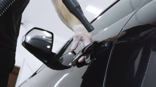 Man washes a brown car at a car wash. Close-up of the Turbo Dryer blowing water off the door handle.