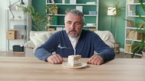 Mature Man with Birthday Cake Blows Out Candle
