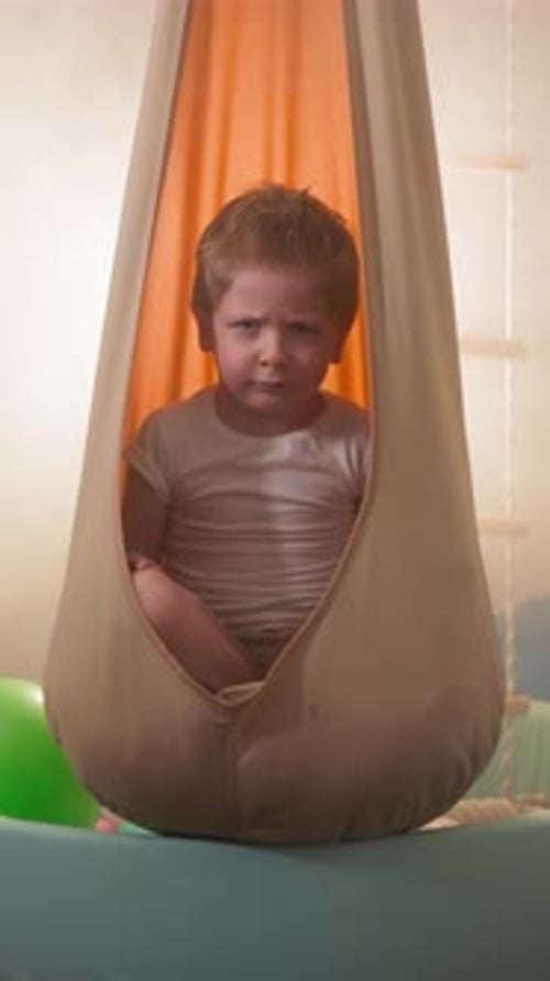 Red-Haired Child Sitting in Fabric Swing Indoors