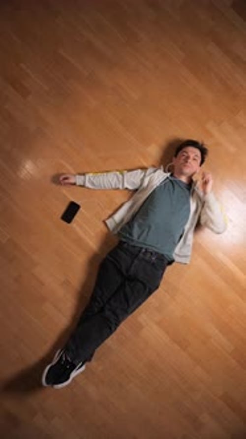 Vertical Video Young Man Unwinding on a Light Wooden Floor Relaxing at Home While Listening to Music
