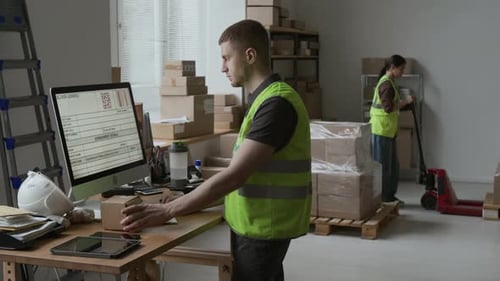 Male Worker in Reflective Vest Entering Parcel Number on Computer in Storeroom