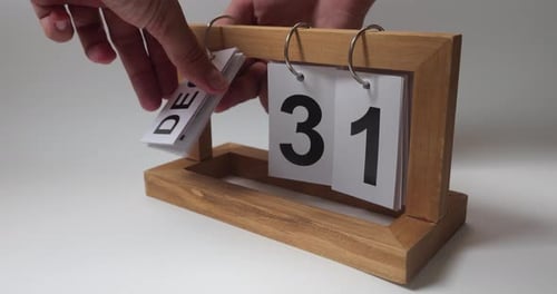 Man's Hands Turn Over the Paper Pendant Calendar on the Marble Table Against White Wall Background