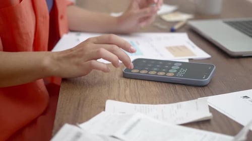 Avec un ordinateur portable à proximité, une femme calcule efficacement les finances du ménage sur son smartphone à un bureau