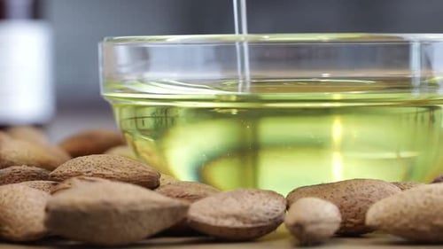 Almond Oil is poured into a bowl. Almonds next to the bowl on the table.