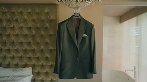 elegant groom suit jacket hanging on chandelier in refined hotel room