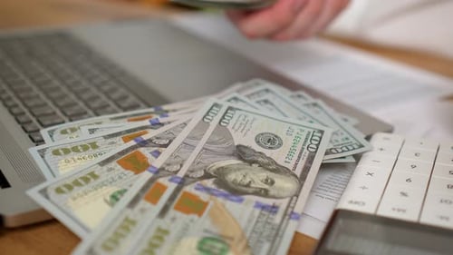 Man Working in Office Counting Dollars Money While Sitting in Front of Laptop Pressing Calculator
