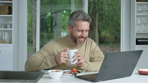 Man Eating Breakfast and Using Laptop in Kitchen