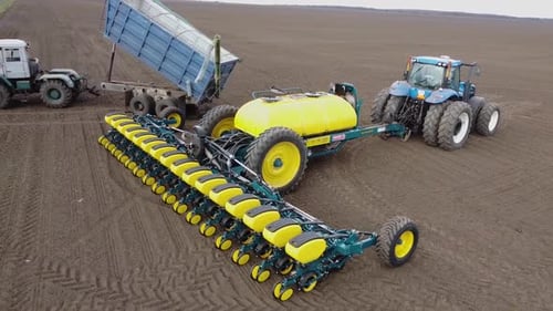 Blue tractor with yellow seeder working on the field in Ukraine OA