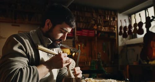 Man Carefully Carving a Violin Scroll in Workshop