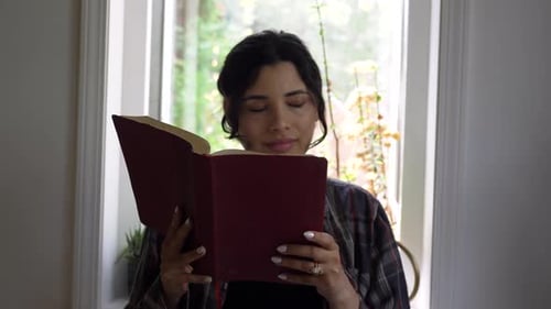 Puerto Rican girl reading holy bible reflecting on religious scripture in front of bright window