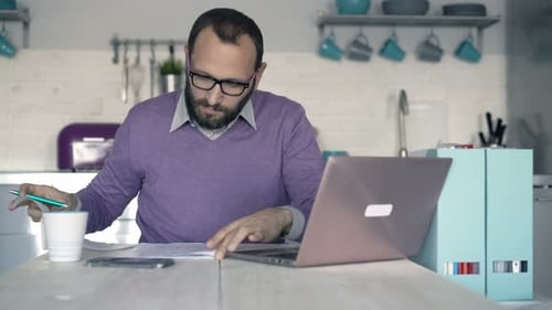 Man Working at Table with Laptop and Documents