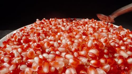 I spread red pomegranate seeds on a plate with a spoon. close-up.