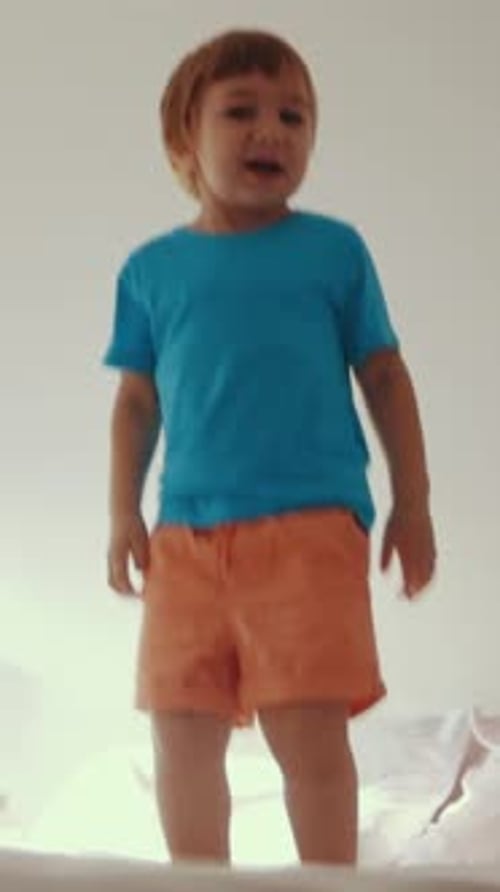 Excited Boy Jumps on Bed in Bright Room