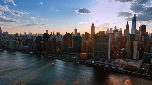 Sun hiding behind the skyline of modern New York. Boats float by the East River. Aerial perspective.