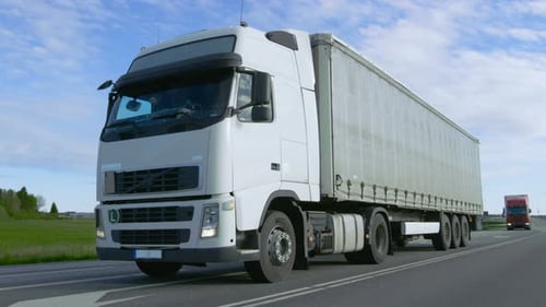 Speeding White Semi Truck with Cargo Trailer Drives on the Highway. Truck is First in the Column of