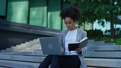 Woman Working on Laptop and Writing in Notebook