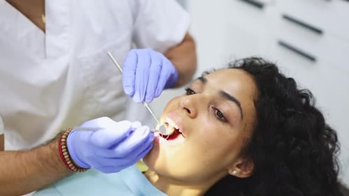 Primer plano de un dentista irreconocible que examina la boca de una paciente femenina en una clínica dental moderna