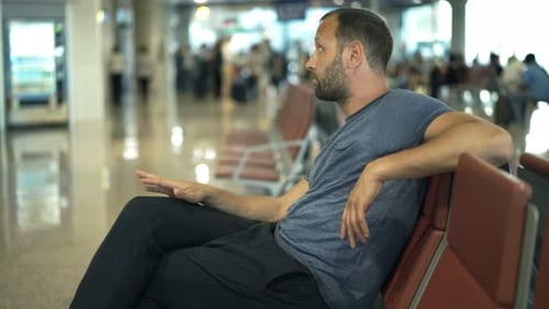 Impatient man awaits delayed flight in busy airport terminal lobby