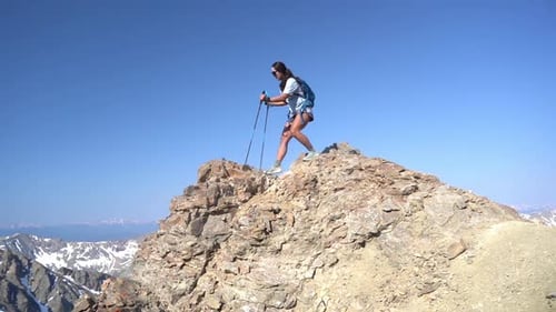 Female Mountaineer on Top of Rocky Summit Walking Carefully With Trekking Poles. Breathtaking View F