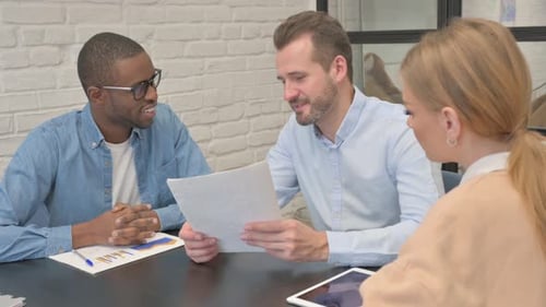 Three Adults Discussing Charts and Documents in Office